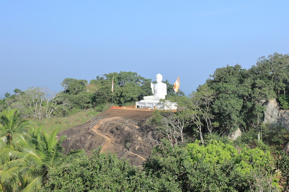 a large white statue sitting on top of a lush green hillside