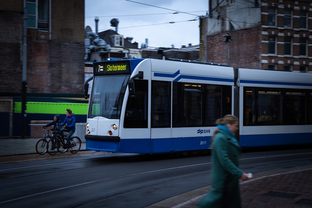 a blue and white train traveling down a street next to tall buildings