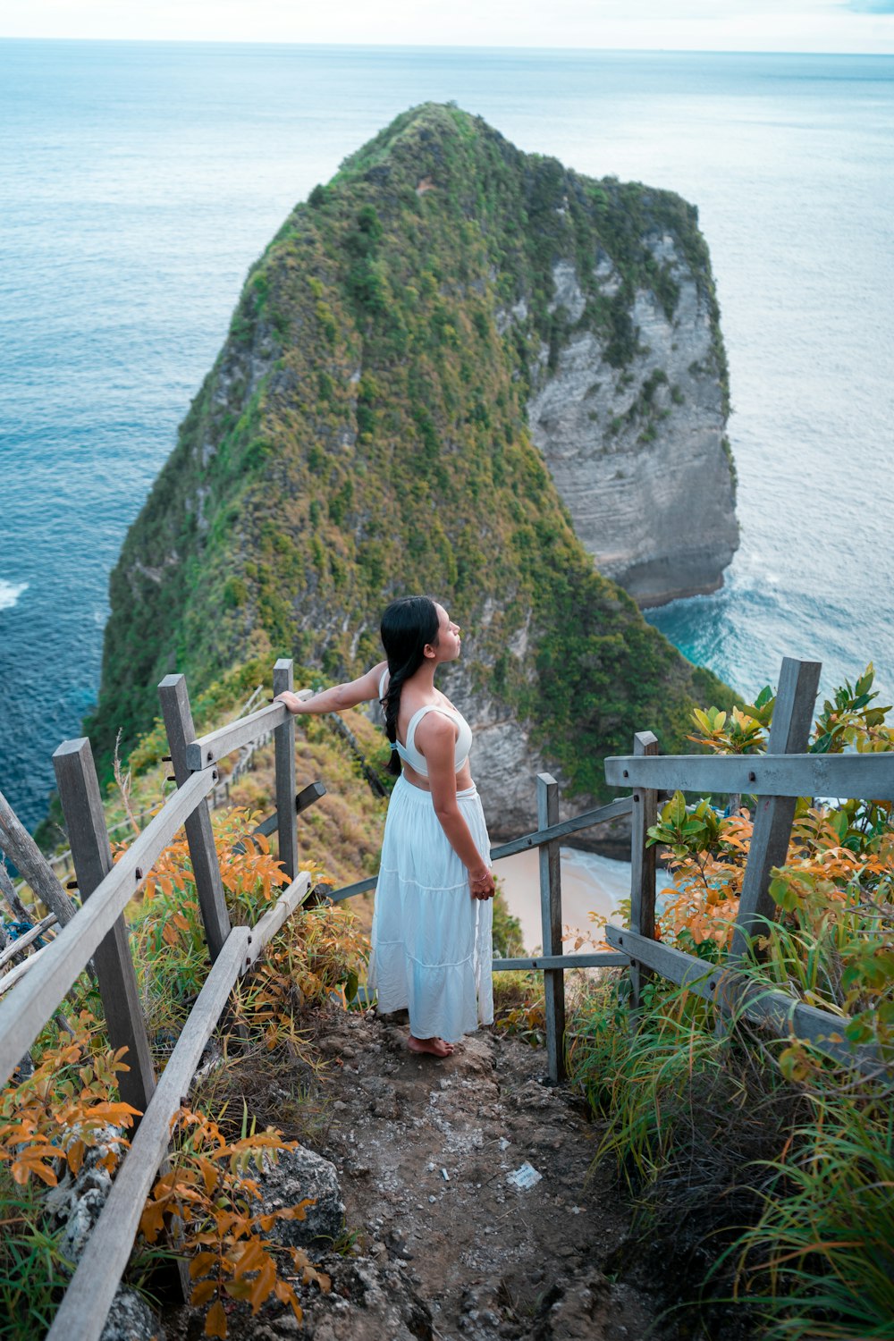 a woman in a white dress standing on a wooden railing