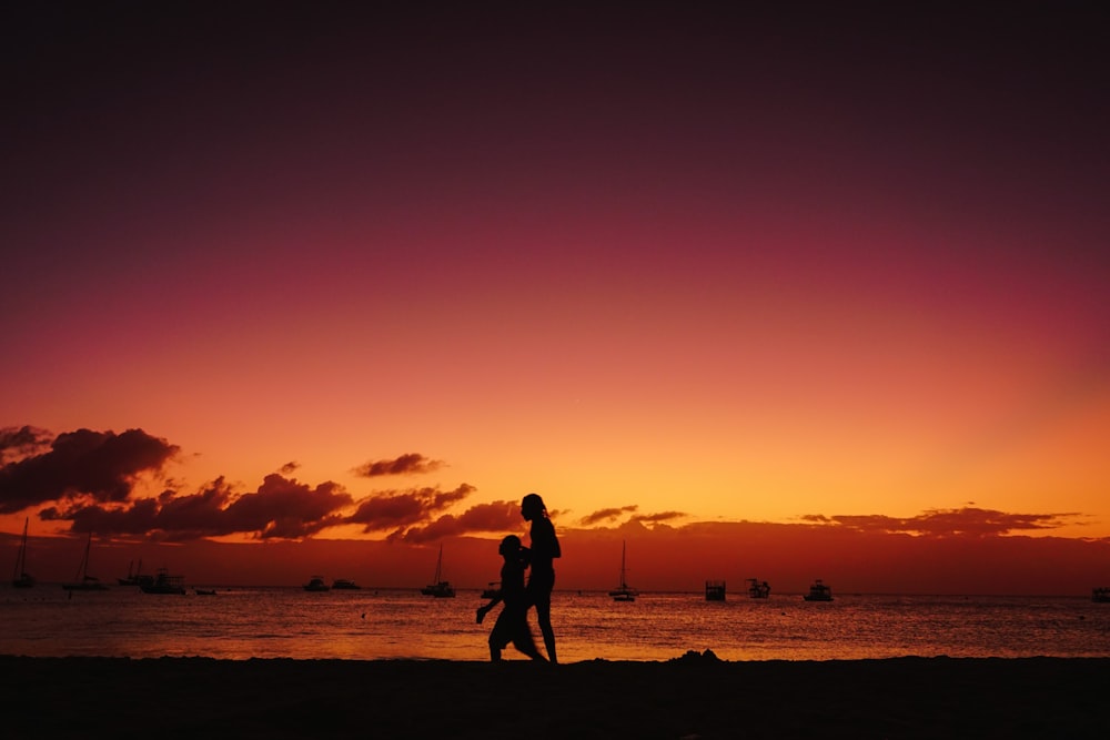 two people walking on a beach at sunset