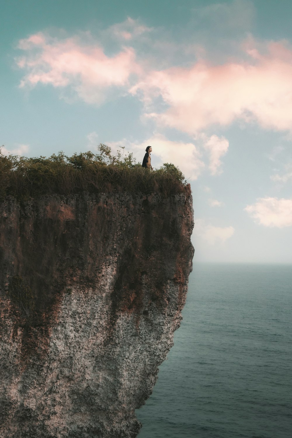 um homem de pé no topo de um penhasco com vista para o oceano