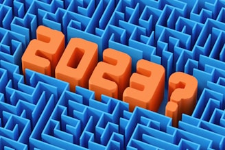 Large, bold orange numbers and a question mark in 3D text appear to rise from a complex blue maze, suggesting uncertainty or questioning related to the year 2023.