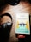 A set of black headphones rests on a wooden surface beside a copy of Jane Austen's 'Pride and Prejudice.' The book cover features an illustration of people standing on a bridge surrounded by tall trees in a contrasting palette of blue, yellow, and white. A small red sticker at the bottom indicates a bargain book sale.
