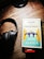A set of black headphones rests on a wooden surface beside a copy of Jane Austen's 'Pride and Prejudice.' The book cover features an illustration of people standing on a bridge surrounded by tall trees in a contrasting palette of blue, yellow, and white. A small red sticker at the bottom indicates a bargain book sale.