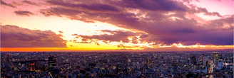 A vibrant city skyline under a dramatic sunset with visible smog layers.