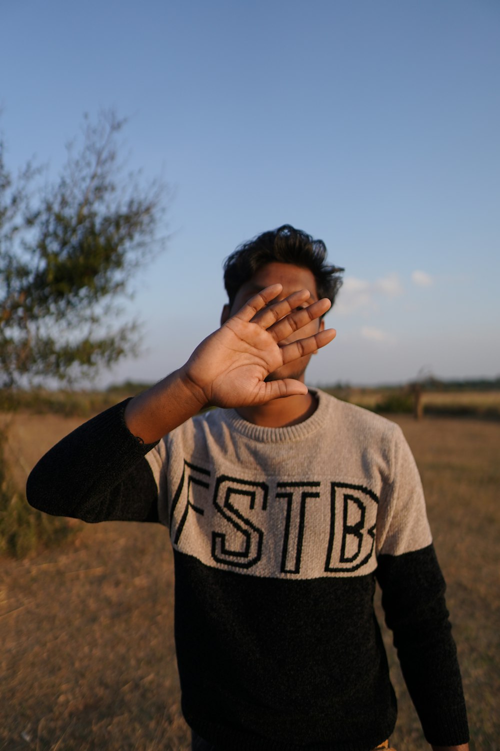 a man standing in a field holding his hands up to his face