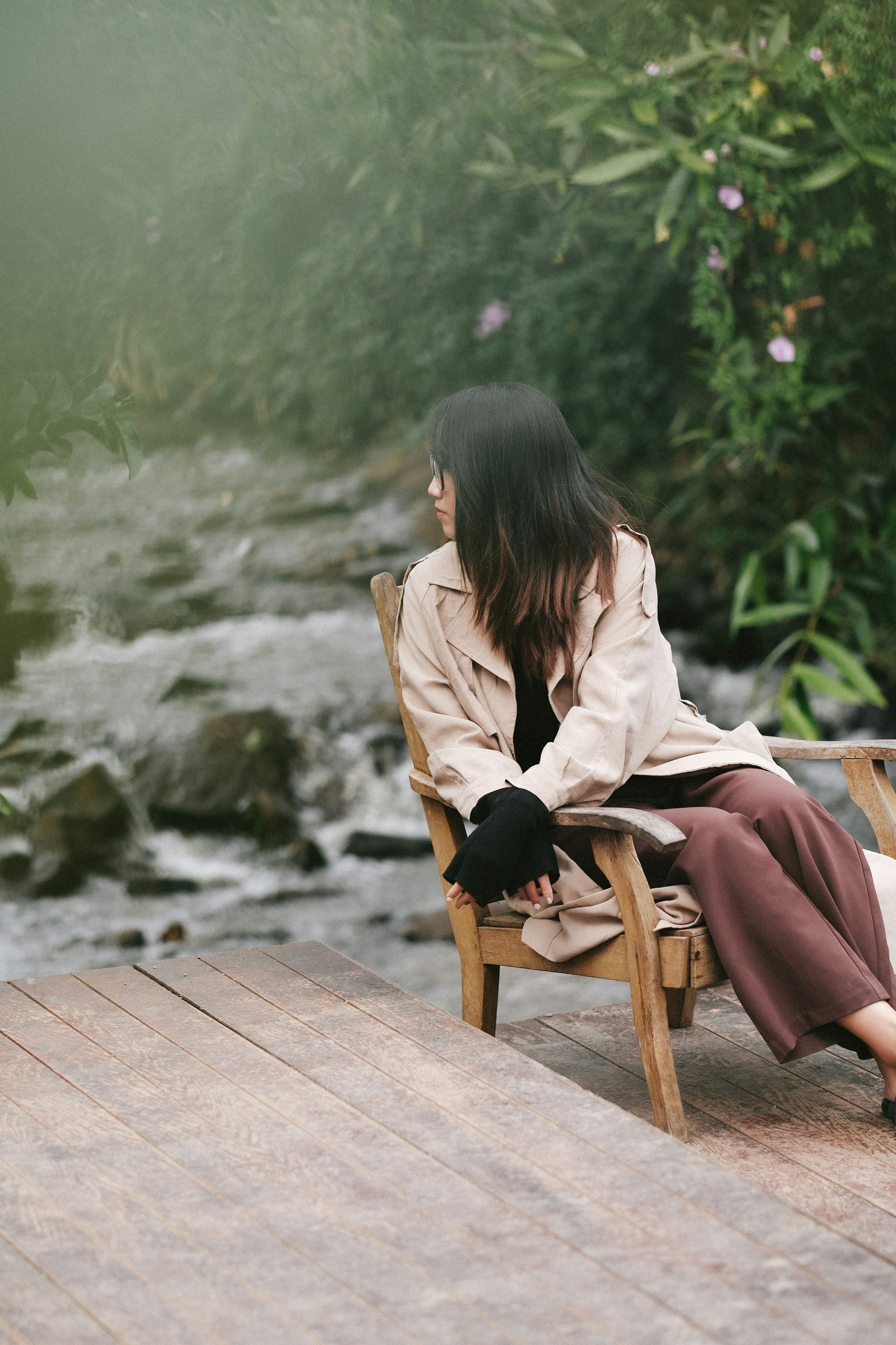 a woman sitting on a wooden chair next to a river