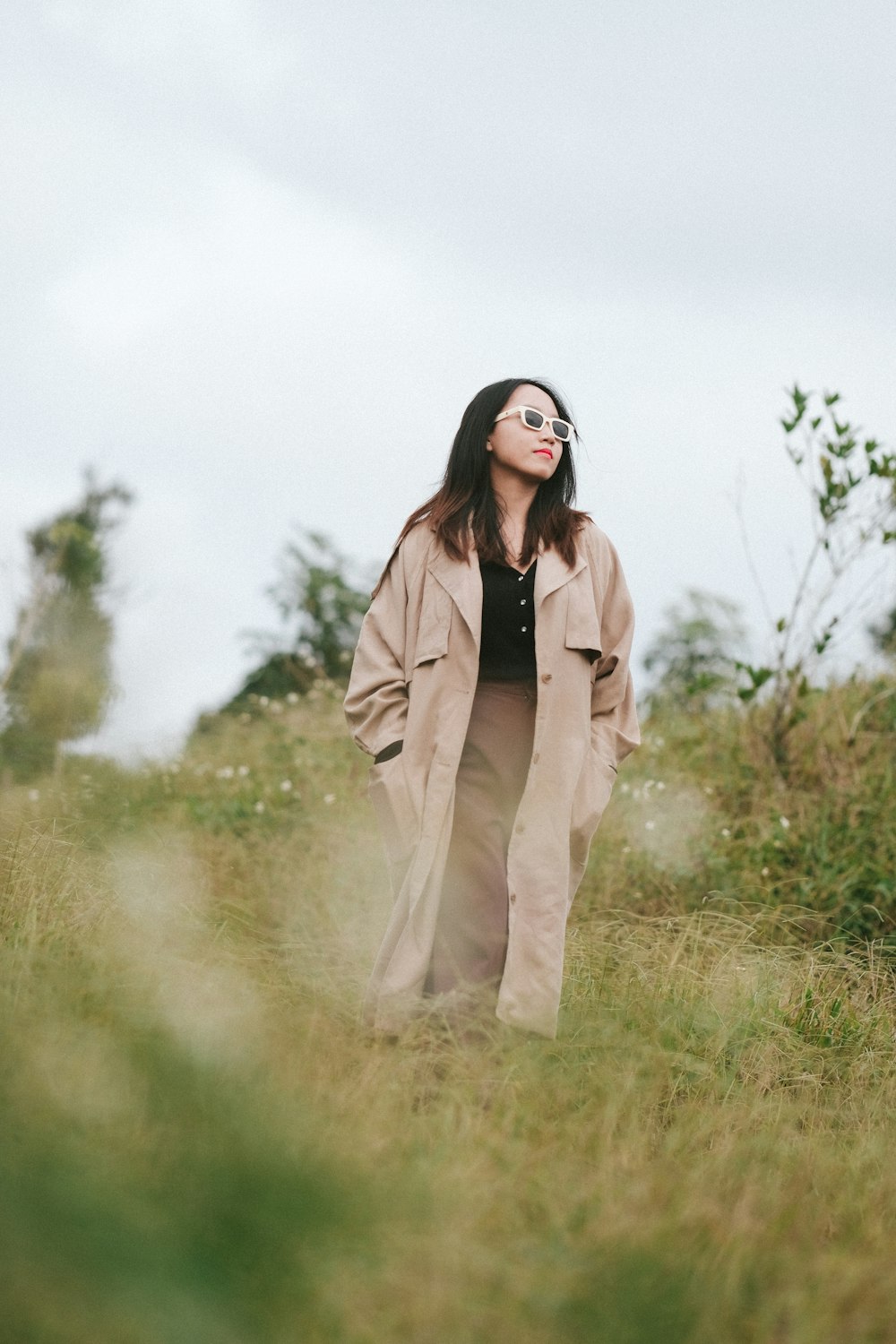 a woman standing in a field wearing a trench coat