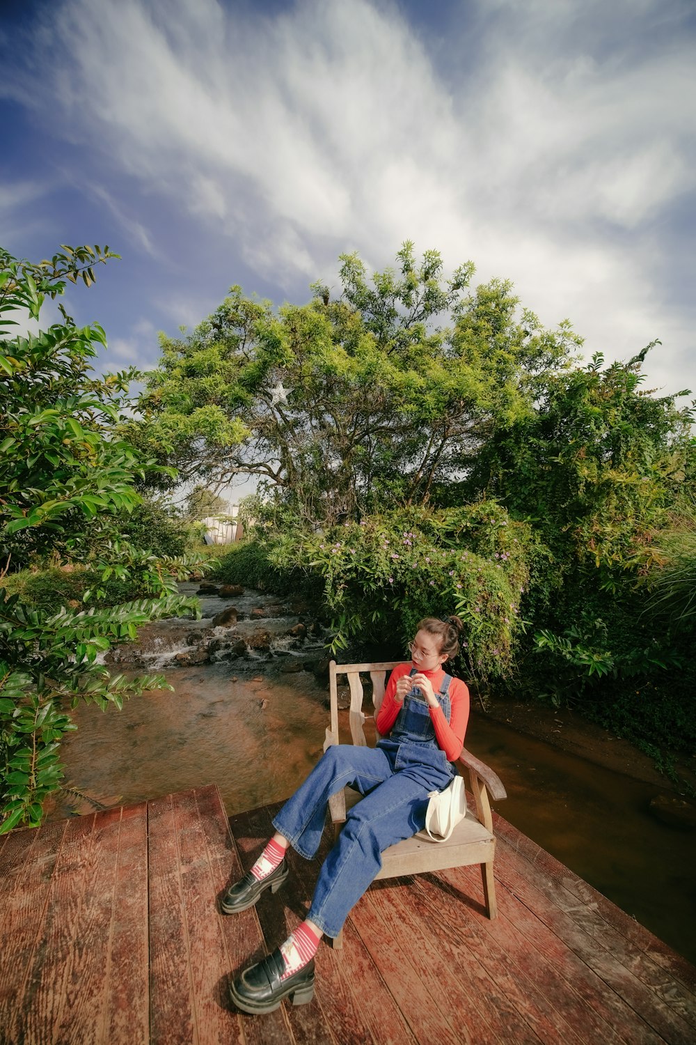 a woman sitting on a wooden bench next to a river