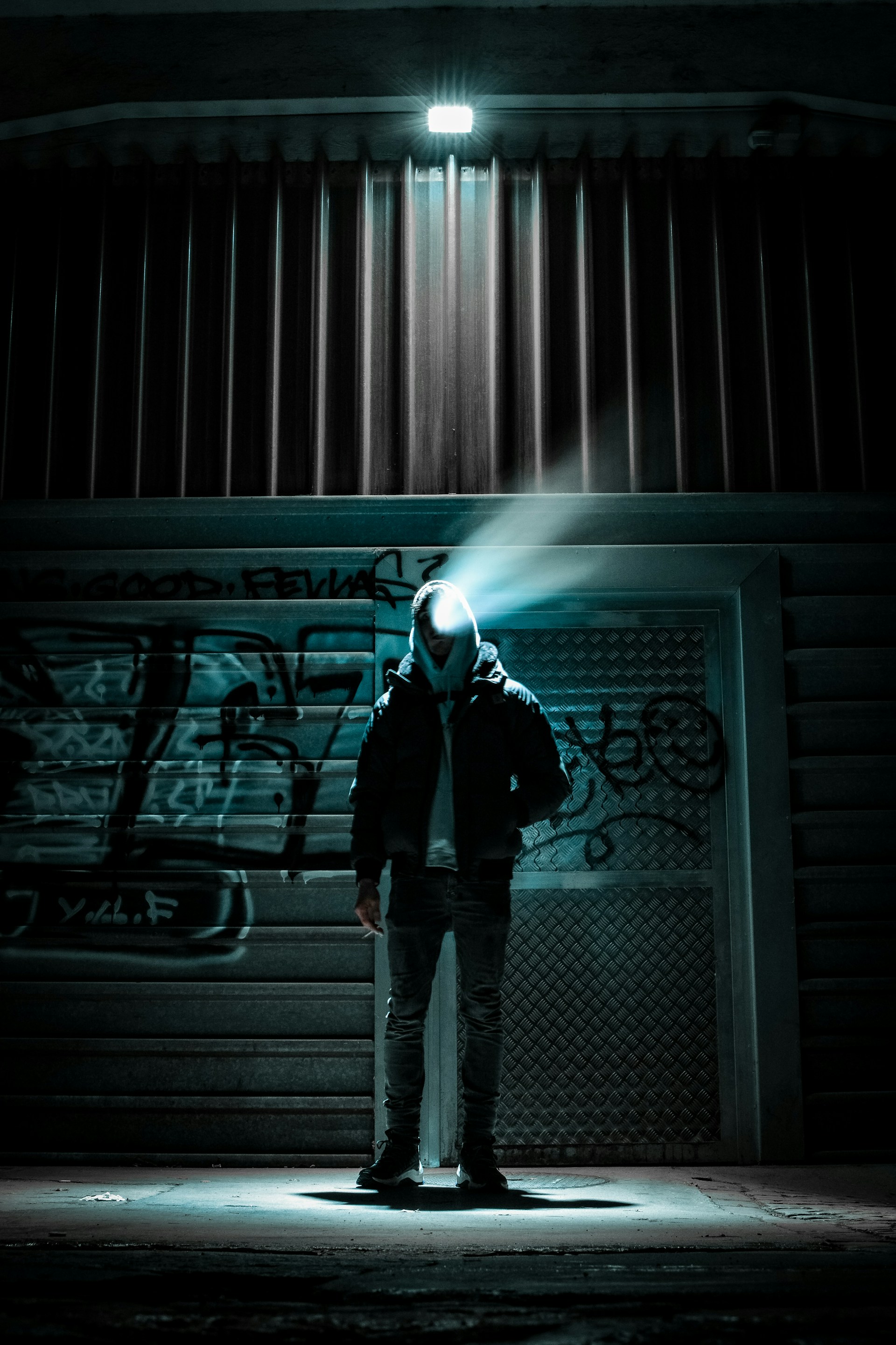 A moody, neon-lit alleyway with a model wearing an oversized black hoodie, glowing cyberpunk tattoos visible under the hood.