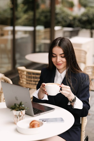 a woman sitting at a table with a laptop and a cup of coffee