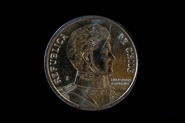 A gold-colored coin featuring the profile of a historical figure. The words 'Republica de Chile' are inscribed along the edges. Details of clothing and embellishments are discernible on the portrait.