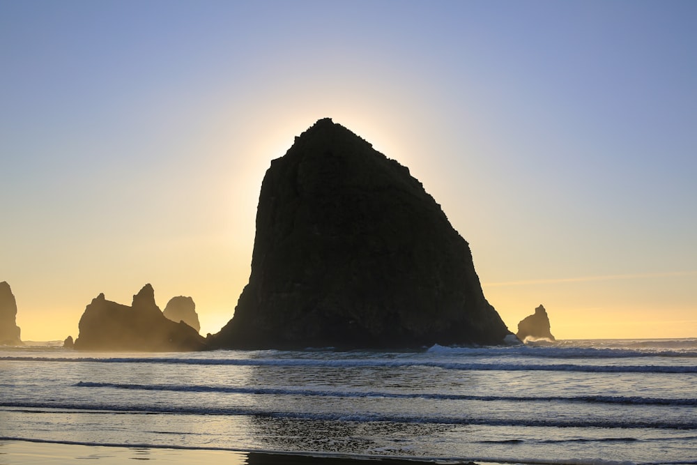 a large rock sticking out of the ocean next to a beach