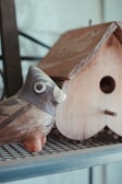 A rustic ceramic ornament shaped like a bird, glazed in earthy tones and perched on a wooden shelf.