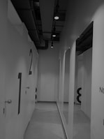 A corridor with numbered doors leading to individual rooms, each marked with large numbers painted on them. The ceiling features exposed ductwork and spotlights, contributing to a modern, industrial aesthetic.