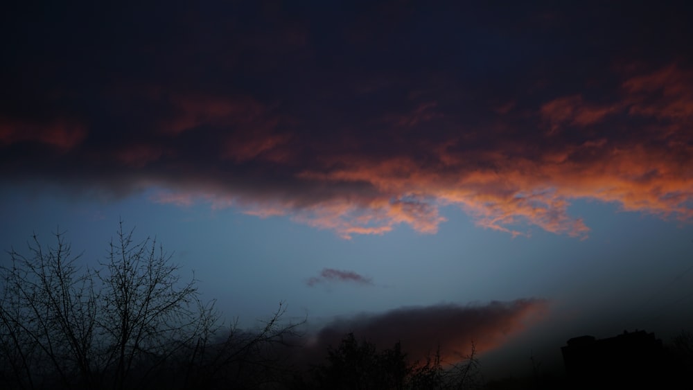 a dark sky with clouds and trees in the foreground