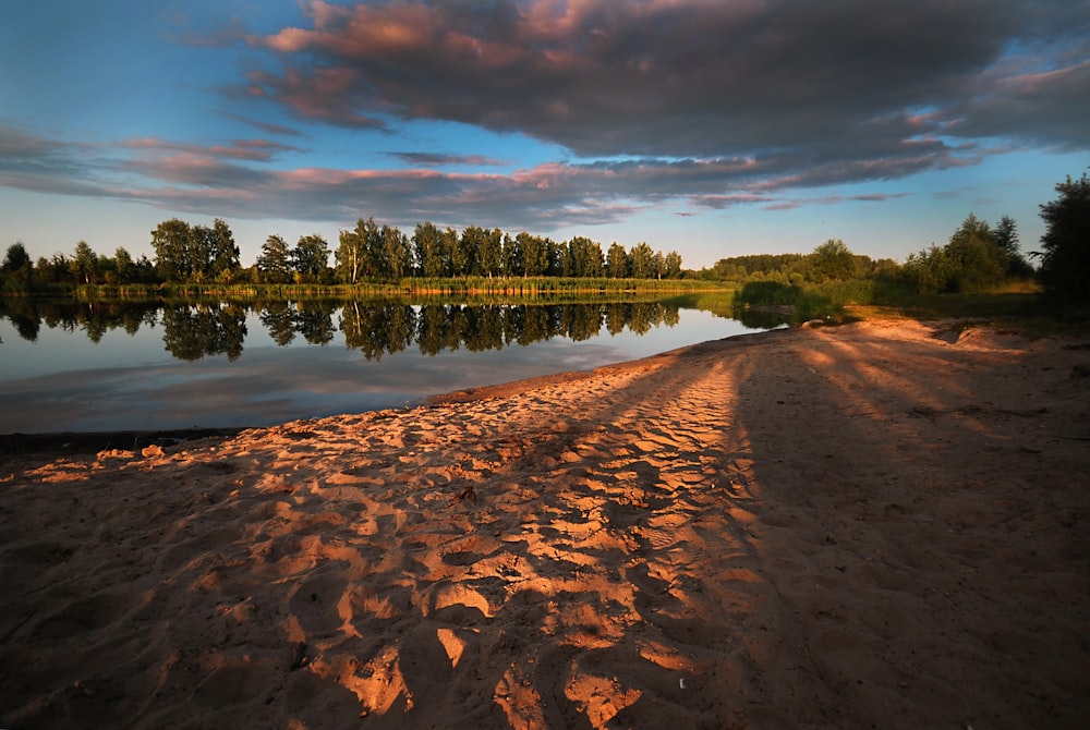 a sandy beach next to a lake under a cloudy sky