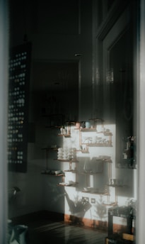 A softly lit interior space with decorative shelves adorned with ceramics and pottery. The light casts shadows on the walls, creating a serene and artistic atmosphere. The arrangement of objects is neat and symmetrical.