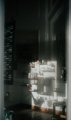 A softly lit interior space with decorative shelves adorned with ceramics and pottery. The light casts shadows on the walls, creating a serene and artistic atmosphere. The arrangement of objects is neat and symmetrical.