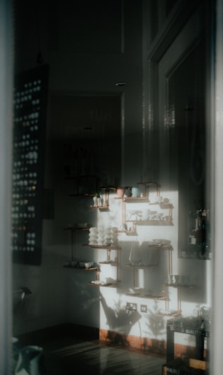 A softly lit interior space with decorative shelves adorned with ceramics and pottery. The light casts shadows on the walls, creating a serene and artistic atmosphere. The arrangement of objects is neat and symmetrical.