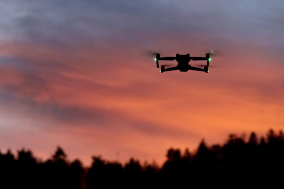 A sleek drone hovering over a solar farm at dusk, with glowing cyan and orange accents highlighting its sensors.