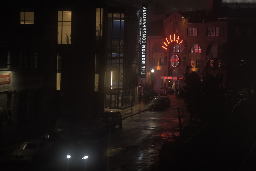 a city street at night with cars parked on the side of the road