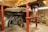 A mechanical setup featuring large interlocking gears supported by red metal pillars. The space has a rustic feel with wooden beams and a brick floor. The machinery appears to be part of an old mill or industrial setting, with visible wear indicating age and usage.
