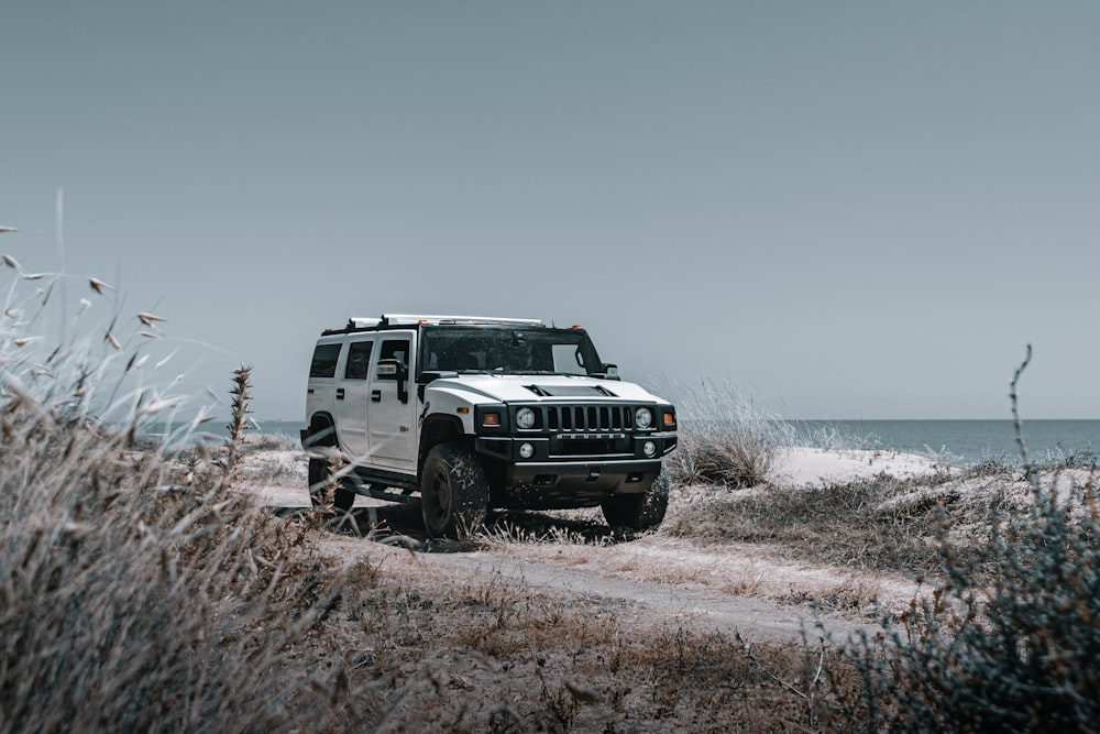 a white jeep driving down a dirt road next to the ocean