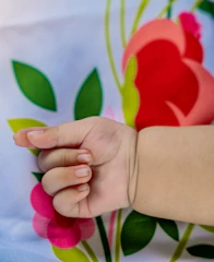 A close-up of a baby’s tiny hands adorned with colorful Munj thread bracelets.