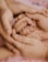 Hands of two adults gently cradling the small hands of a child, conveying a sense of protection and care.