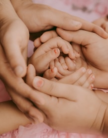 Hands of two adults gently cradling the small hands of a child, conveying a sense of protection and care.