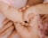 A close-up view of three hands, one belonging to a baby being gently held by an older child and an adult. The focus is on the tenderness and connection between the hands, with the baby's hand grasping a small black object.