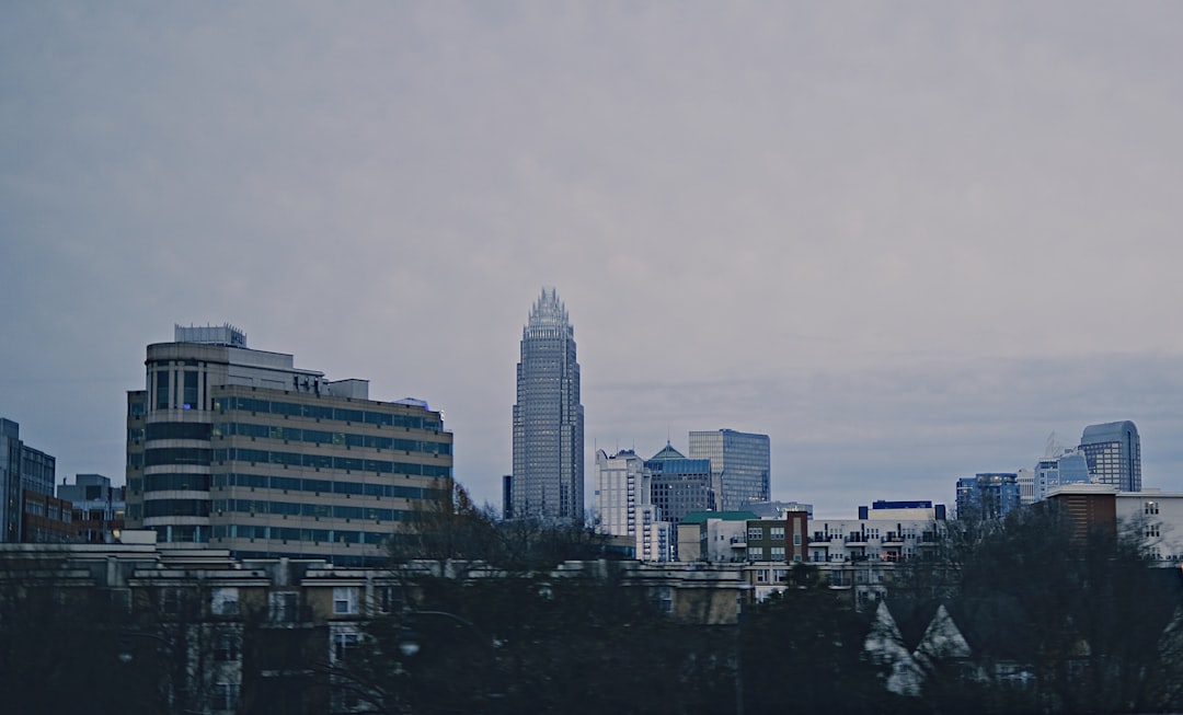 a plane flying over a city with tall buildings, The downtown skyscrapers in Charlotte with overcast sky.