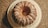 A round bundt cake with a drizzle of white icing on top, placed on a white plate. The cake is set on a textured countertop, creating a contrast with its smooth icing. The icing is unevenly spread, adding a sense of homemade charm.
