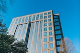 Close-up of a commercial office building with reflective windows and greenery around.