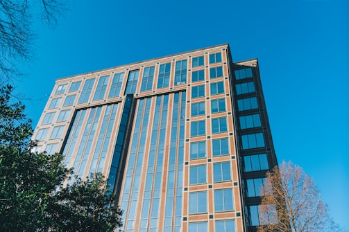 Close-up of a commercial office building with reflective windows and greenery around.