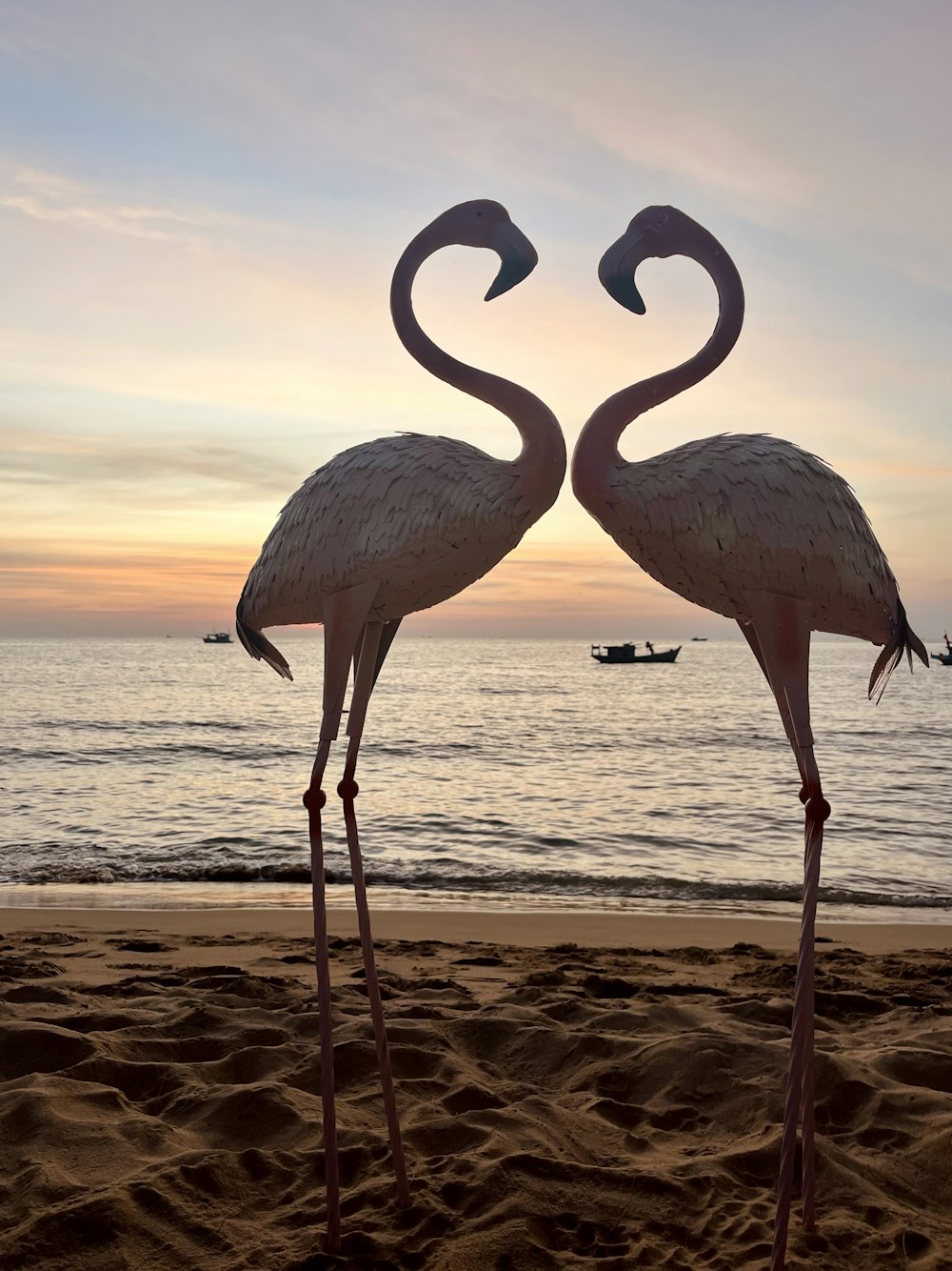 two flamingos standing in the sand on a beach