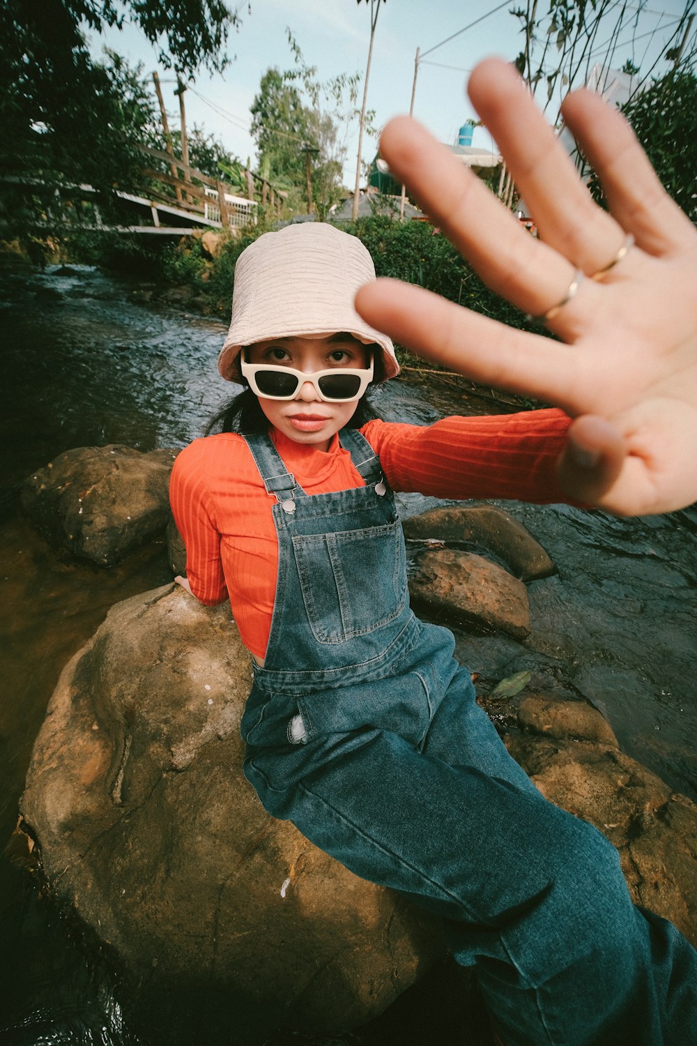 a person wearing overalls and a hat sitting on a rock