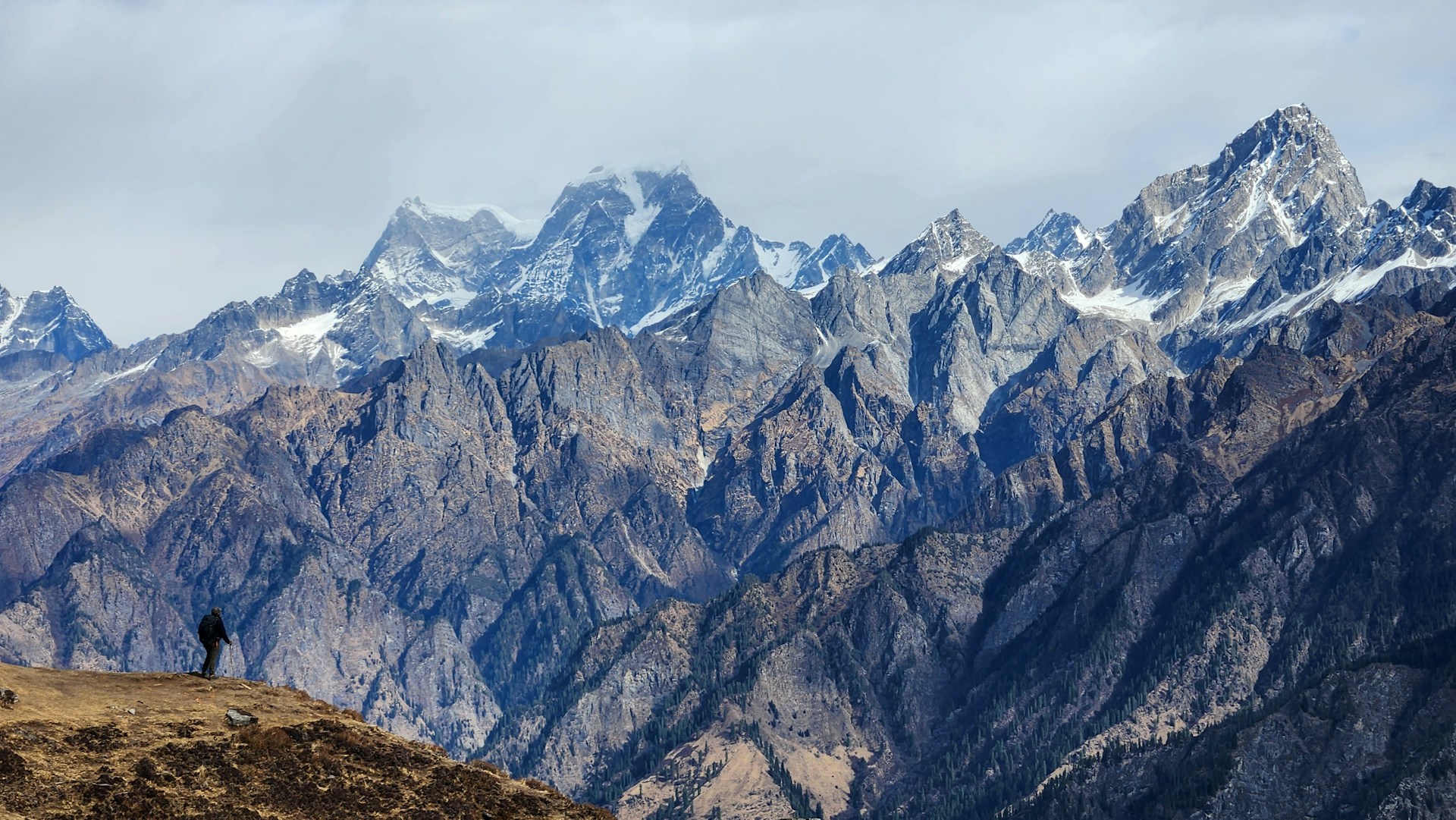 Snow-capped peaks of the Nepalese Himalayas under a clear sky, with a lone traveler standing on a ridge, taking in the breathtaking panorama.
