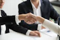 two people shaking hands in front of a laptop