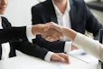 two people shaking hands in front of a laptop