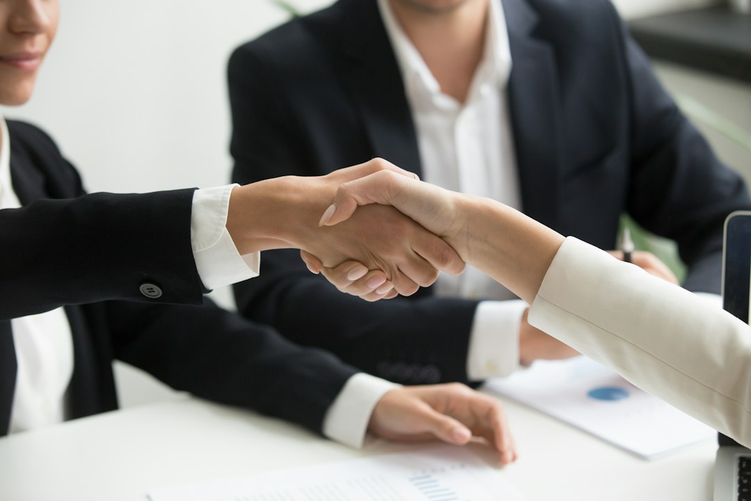 Two professionals shaking hands over a laptop after signing a new client agreement