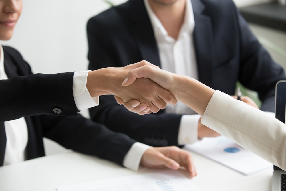 two people shaking hands in front of a laptop