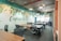 An open office workspace featuring several desks with ergonomic chairs. The walls are decorated with a nature-themed mural and the phrase 'Capture the Nature' is prominently displayed. Overhead, modern light fixtures and exposed ductwork add an industrial touch. Natural light filters in through large windows, enhancing the workspace.