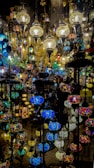 A collection of intricately designed hanging lamps with colorful stained glass and ornate metalwork. The lamps vary in size and shape, casting a warm and vibrant glow with their multicolored patterns.