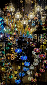 A collection of intricately designed hanging lamps with colorful stained glass and ornate metalwork. The lamps vary in size and shape, casting a warm and vibrant glow with their multicolored patterns.