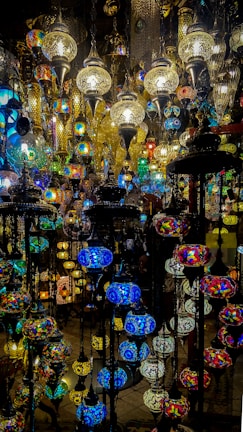 A collection of intricately designed hanging lamps with colorful stained glass and ornate metalwork. The lamps vary in size and shape, casting a warm and vibrant glow with their multicolored patterns.
