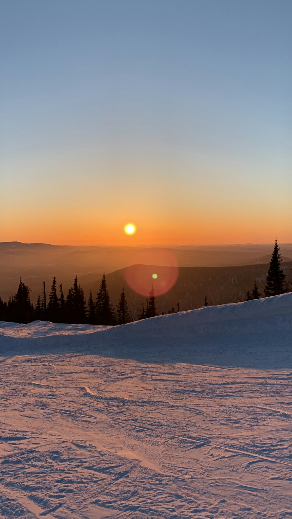 the sun is setting over a snowy mountain