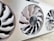 A close-up view of a computer graphics card with three large, white cooling fans enclosed in a metallic casing. The central fan has a visible logo and intricate blade design.
