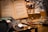 A vintage setting featuring an open book with text in a foreign language. Several magnifying glasses with different handle designs are spread out on a wooden surface. In the background, ornate pens are arranged in a white holder, creating a cozy, scholarly atmosphere.